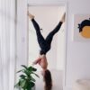 woman in workout gear hanging upside down on doorway near green plants