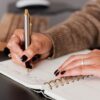 crop woman writing down notes in diary