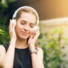 woman wearing black sleeveless dress holding white headphone at daytime